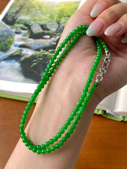 Green jadeite beaded necklace draped on hand with silver clasp charm visible.