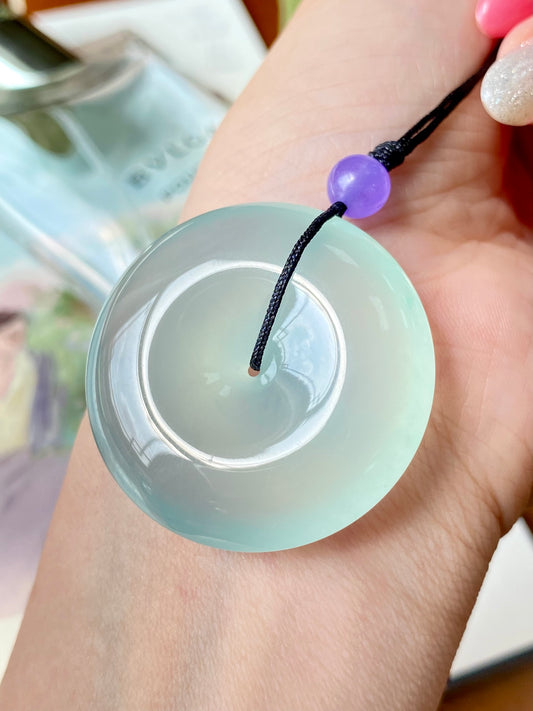 Mint green jade disc pendant held in hand, black cord with purple bead