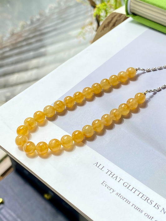 Golden-yellow round bead necklace with silver-toned chain on display stand, side angle
