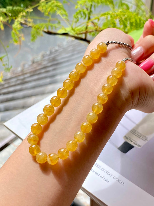 Golden-yellow beaded necklace with silver-toned chain clasp, held in hand