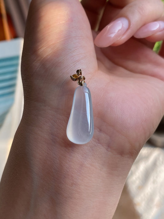 Pale blue jadeite drop pendant with gold decorative bail, close-up on hand