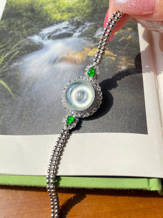 Silver chain bracelet with icy white donut pendant, blue center, green accent stones