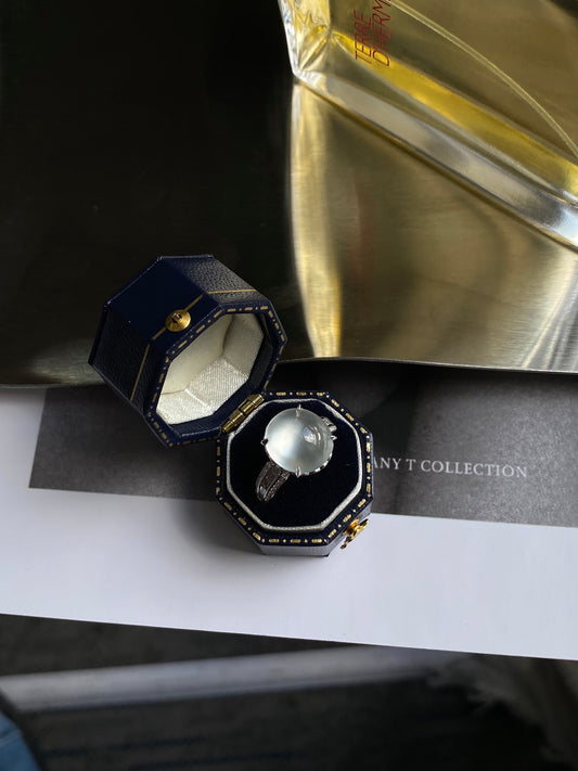 White jadeite cabochon ring shown in open presentation box with dark setting