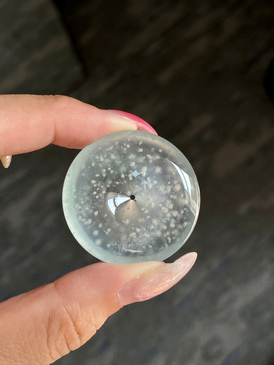 Round jadeite safety disc with speckled snowflake-like inclusions, central pin.