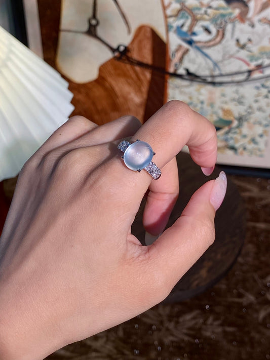 Light-blue cabochon ring on finger with silver prong and halo detailing