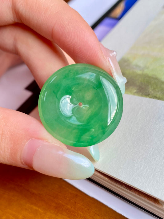 Tilted green jadeite donut, unmounted round stone with central hole; polished translucent