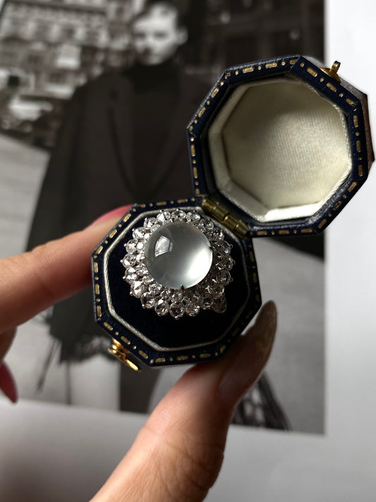 White jadeite cabochon ring beside open blue octagonal jewelry box