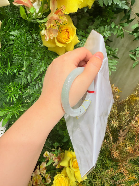 Misty-green round-bar jadeite bangle held against a white package bag