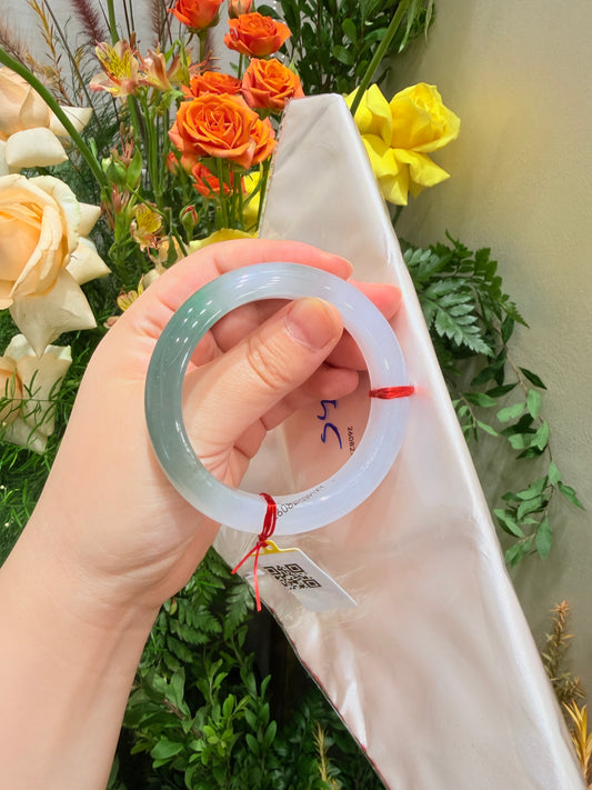 Light blue translucent bangle, close-up in hand, red string and tag visible