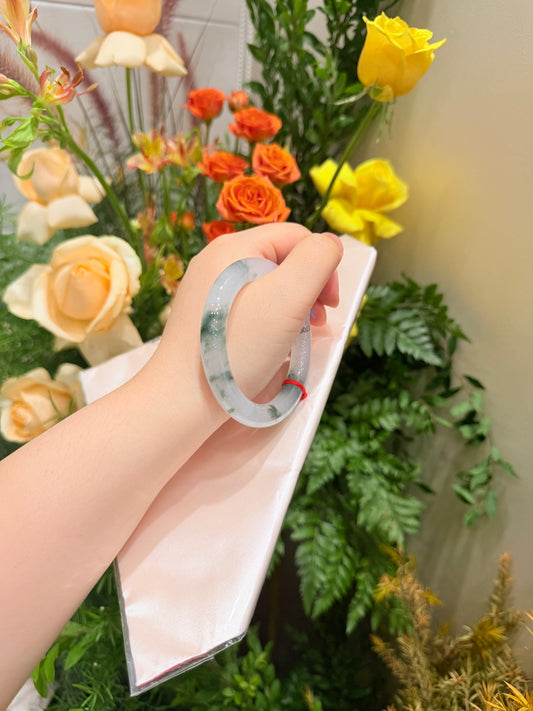 Translucent pale jade bangle bracelet held in hand, circular hoop with speckles