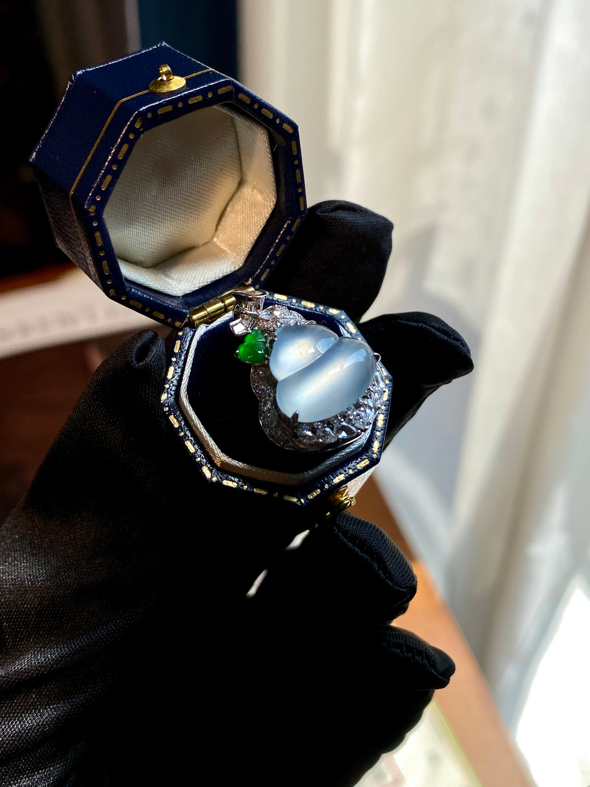 Jade gourd pendant shown in open jewelry box, icy white cabochon with green accent