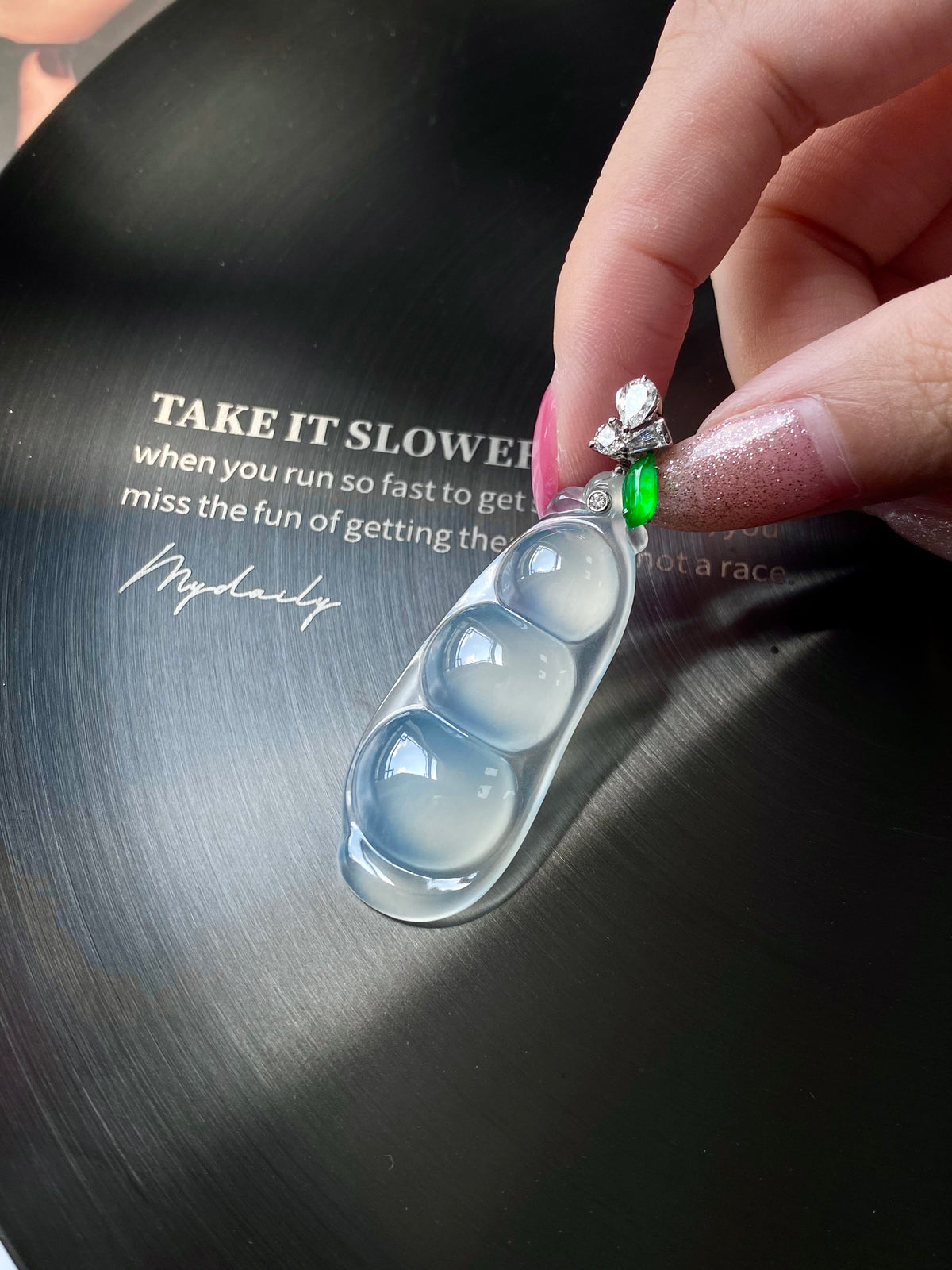 Icy white jadeite pea pod pendant held in hand, green stone and crystal flower detail