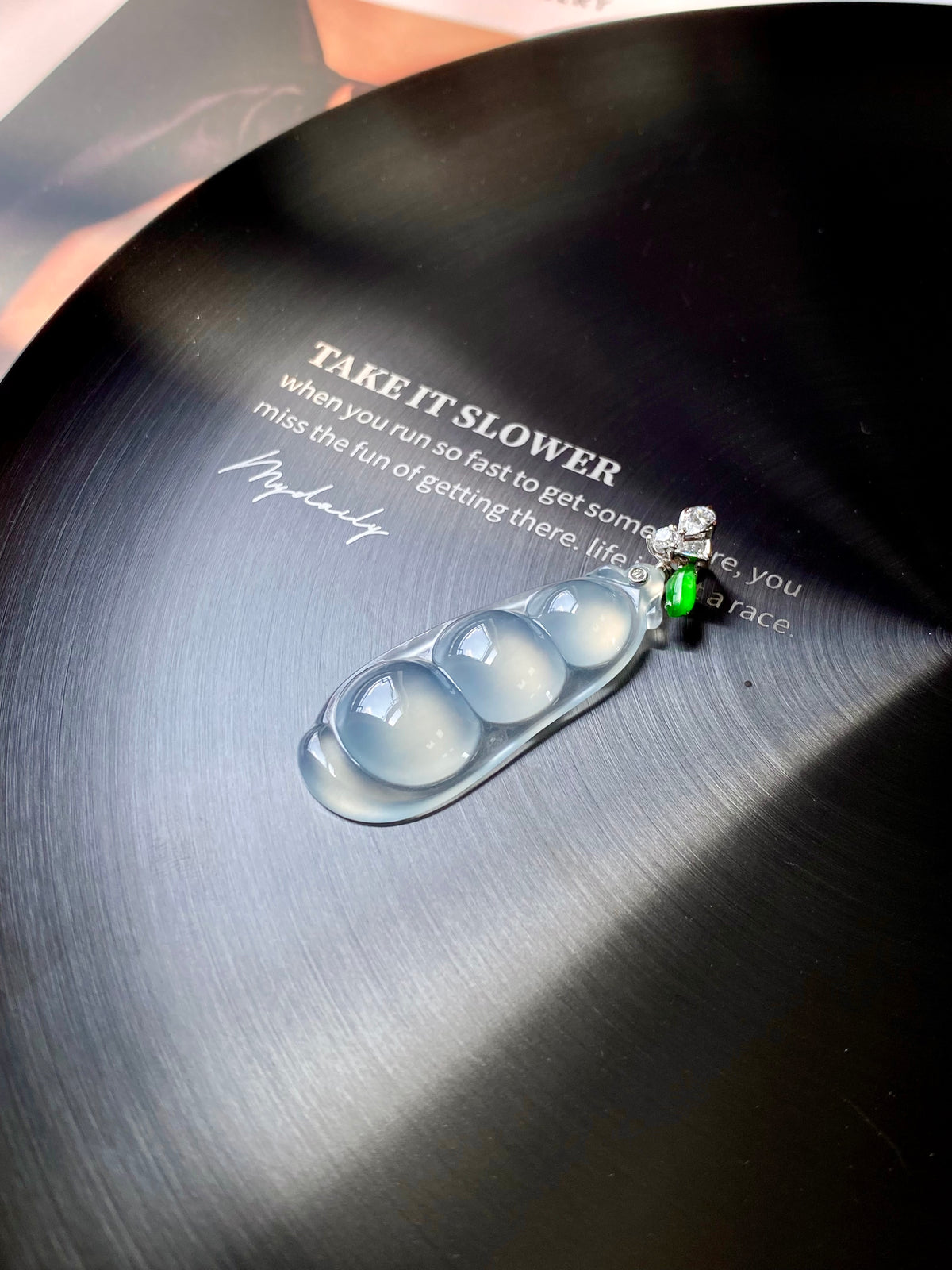 Icy white jadeite pea pod pendant on dark card, green stone and clear crystal flower