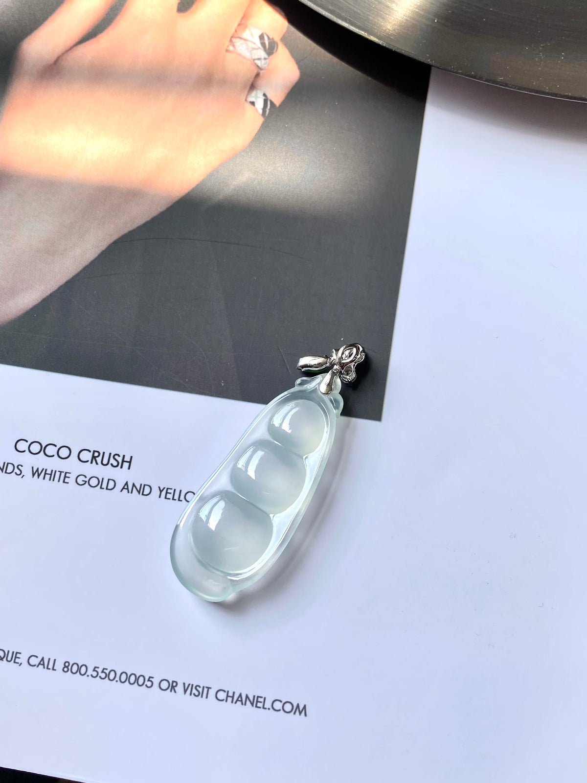 Icy white jadeite pea pod pendant lying flat, green gem and crystal flower detail