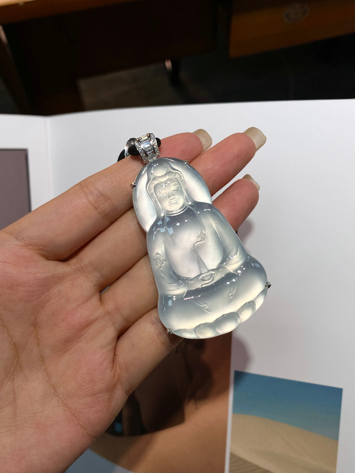 Guanyin pendant with silver-toned bail held in palm; translucent light blue-white glow