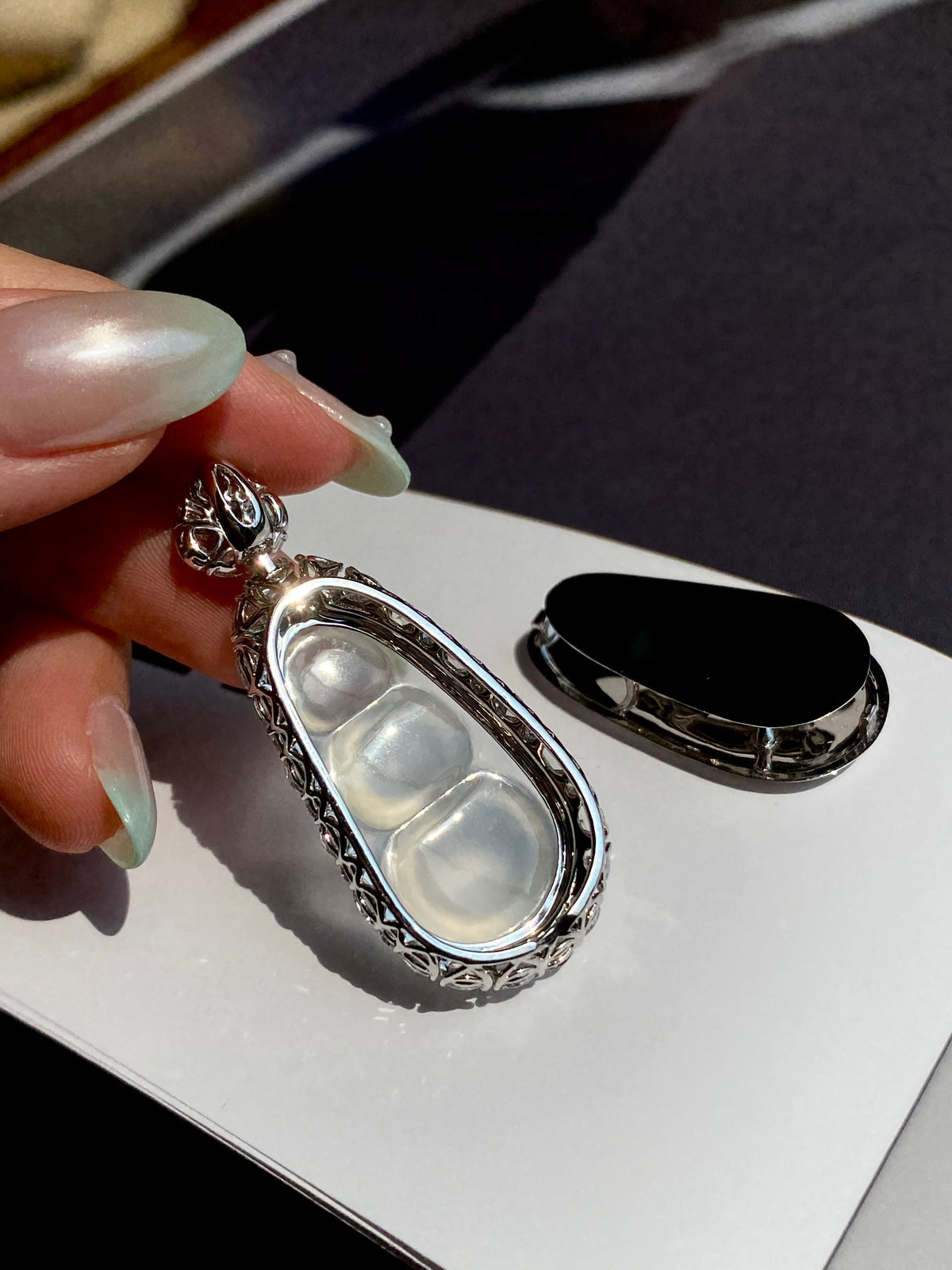 Silver jadeite pea pod pendant with green top stone held over a display card