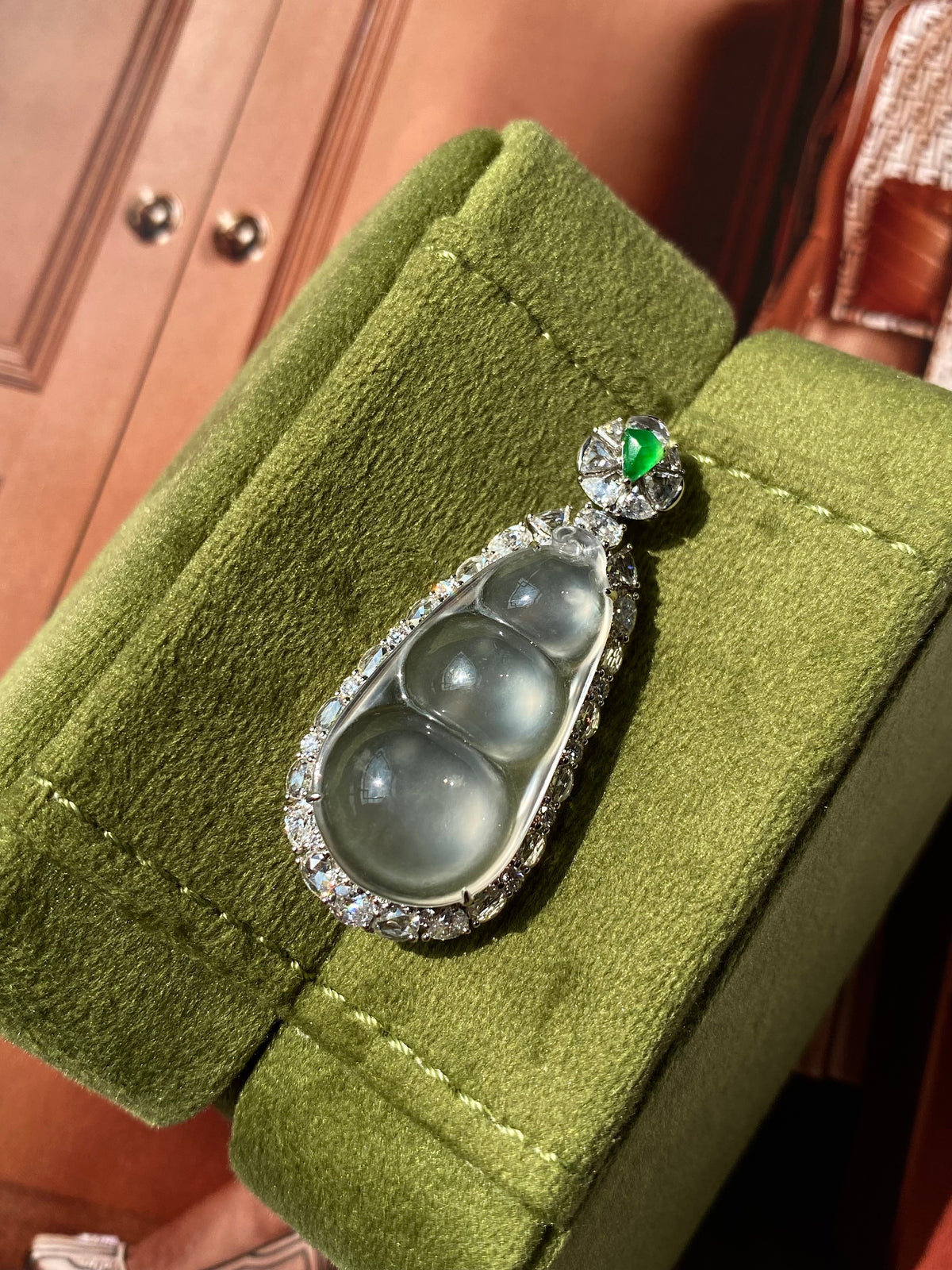 Icy jadeite pea pod pendant with green accent stone in silver setting on green velvet