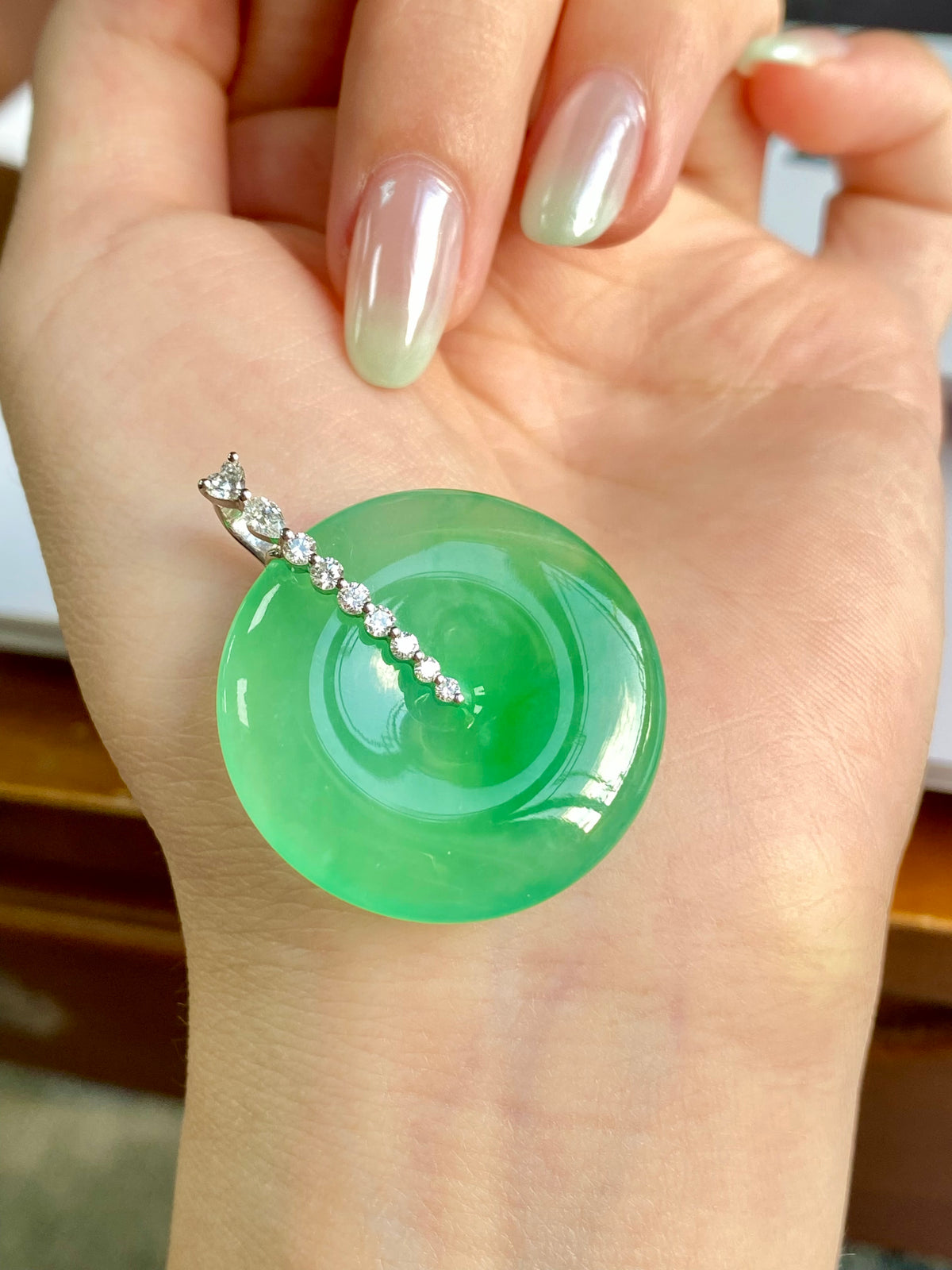 Green jadeite donut pendant on open palm with silver chain of small stones
