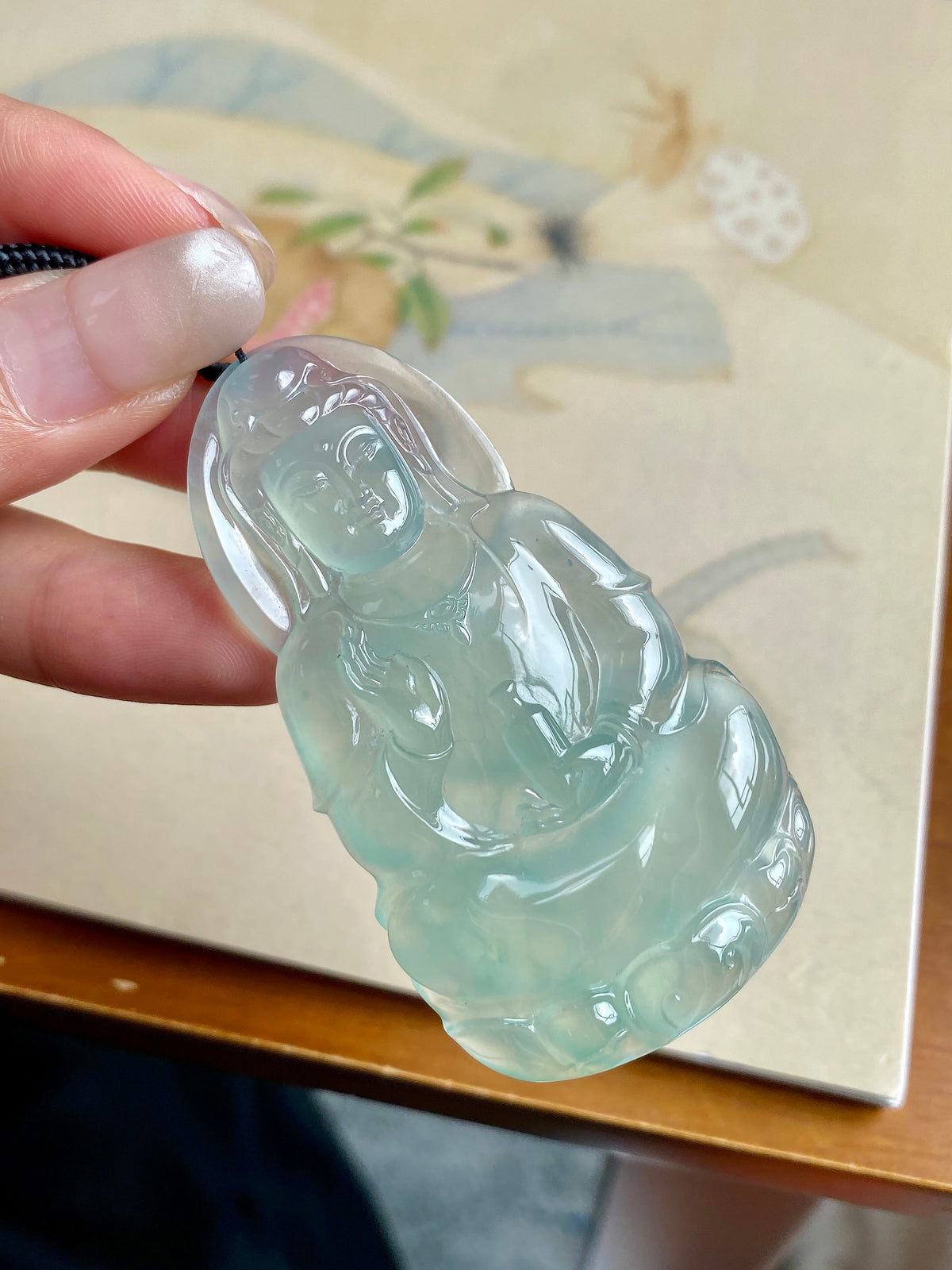 Light green jadeite Guanyin pendant in hand, angled front view with black cord