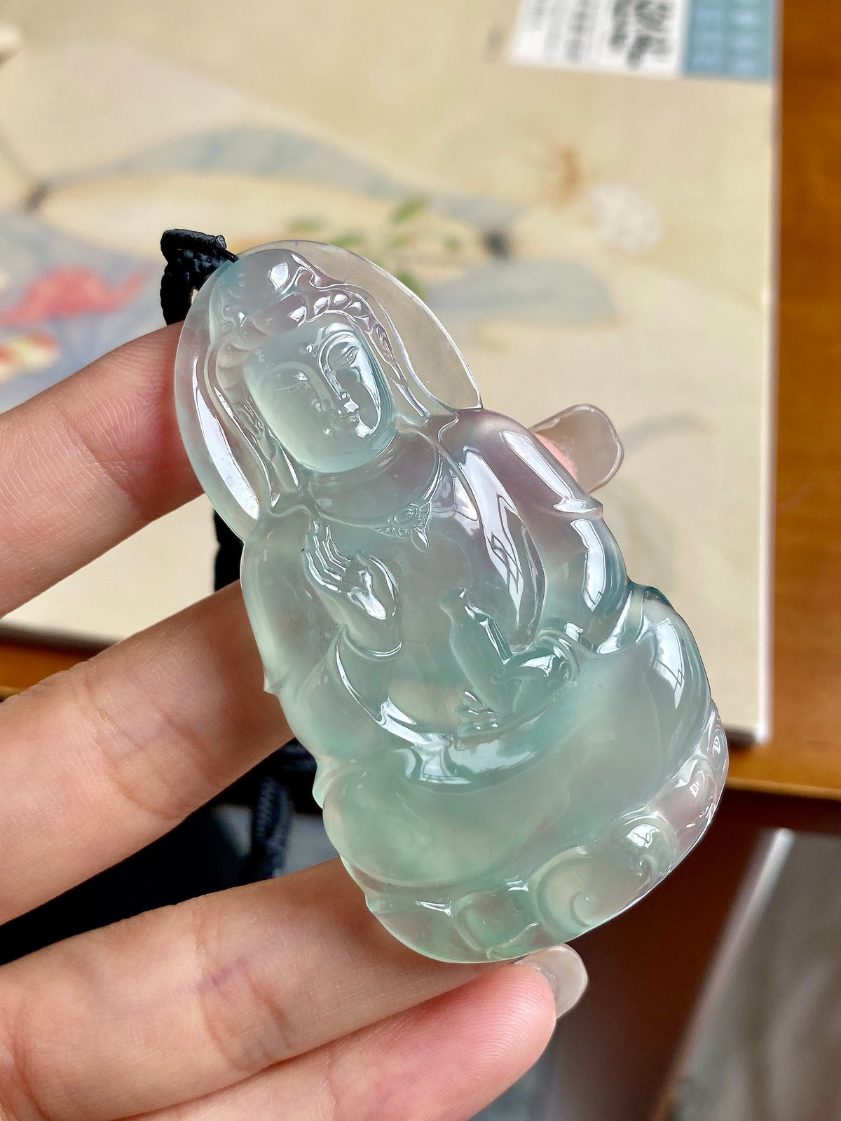 Light green jadeite Guanyin pendant angled view in hand with black cord