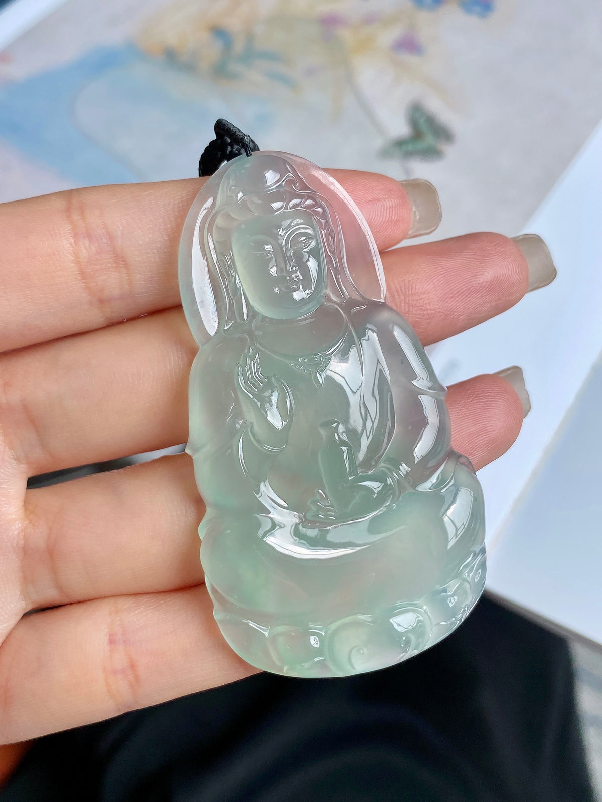 Light green jadeite Guanyin pendant front view on palm with black cord