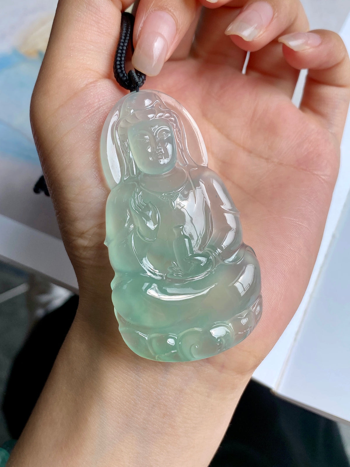 Light green jadeite Guanyin pendant close-up with black cord in hand