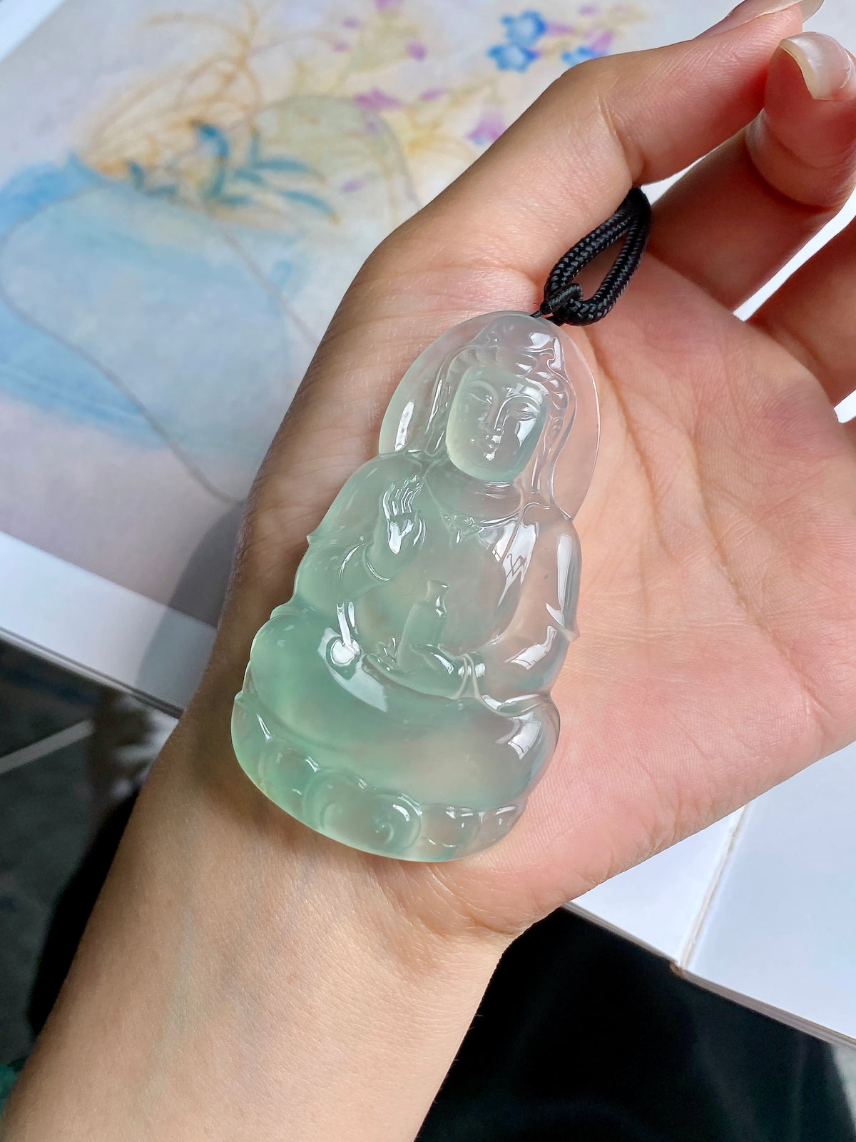 Light green jadeite Guanyin pendant close-up on open palm with black cord