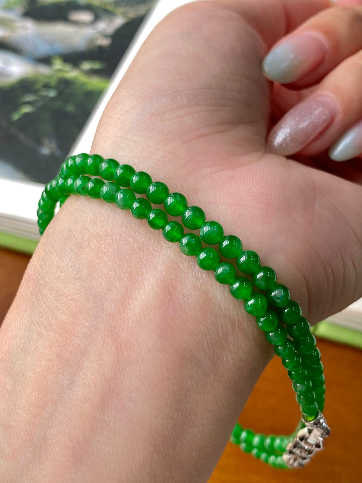 Green jadeite beaded necklace with silver end clasp, shown on wrist.