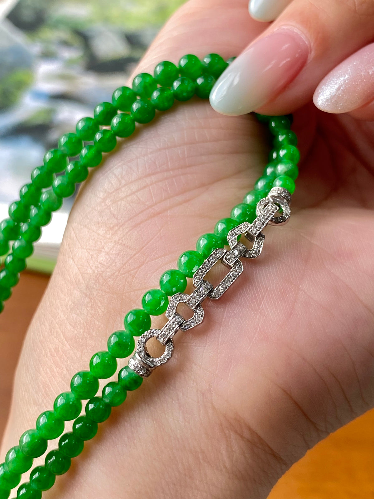 Green jadeite beaded necklace with silver link clasp detail, close-up on hand.