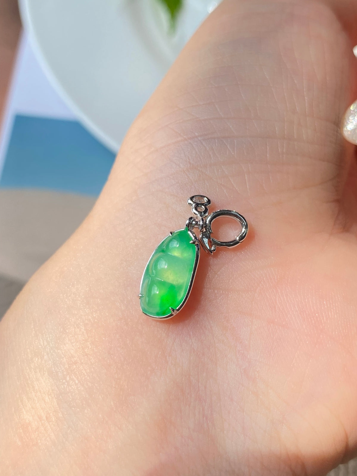 Green jadeite bean pendant with silver bail, shown in close-up on hand