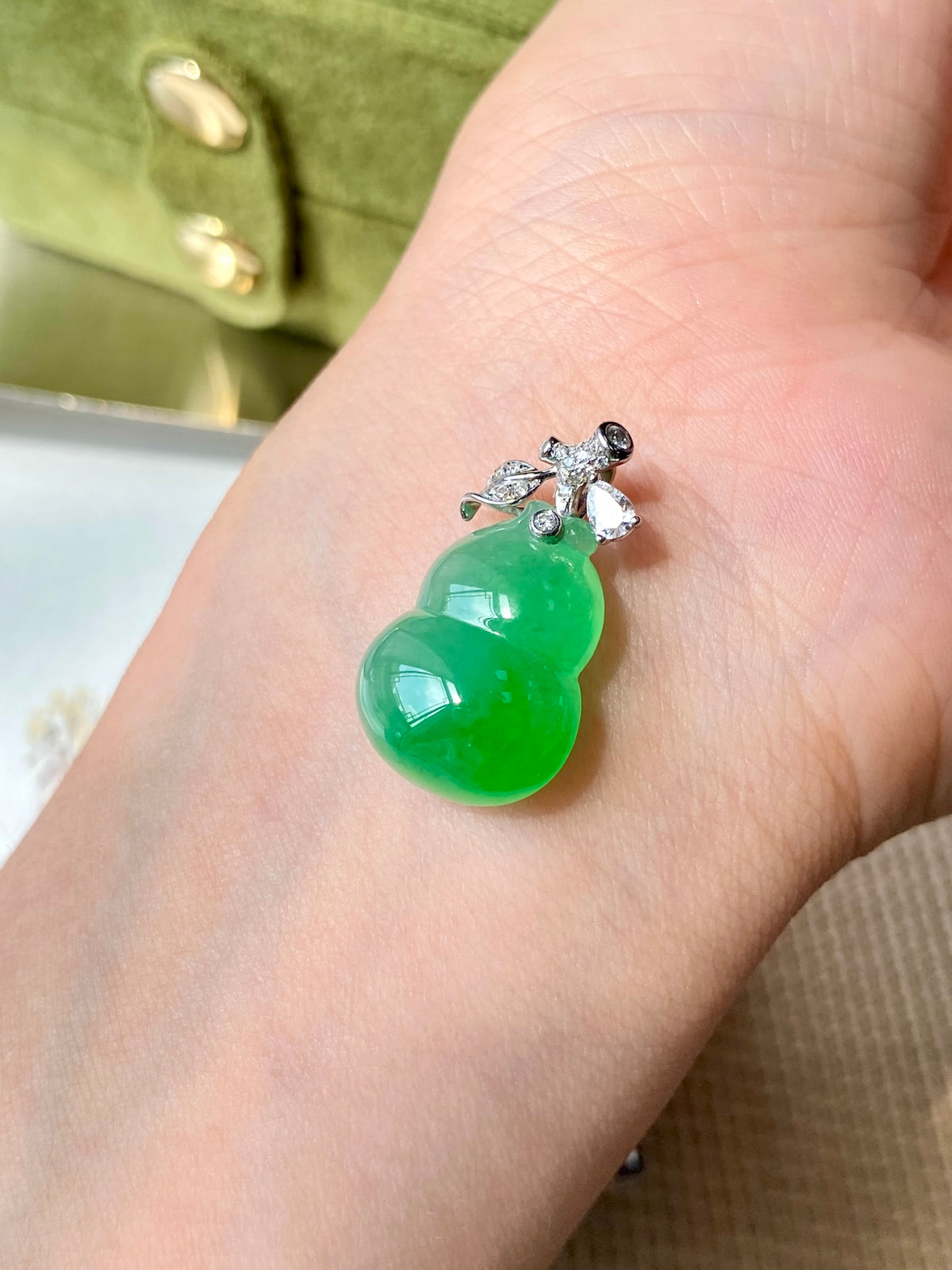 Green jadeite gourd pendant shown on open palm, crystal-set silver bail