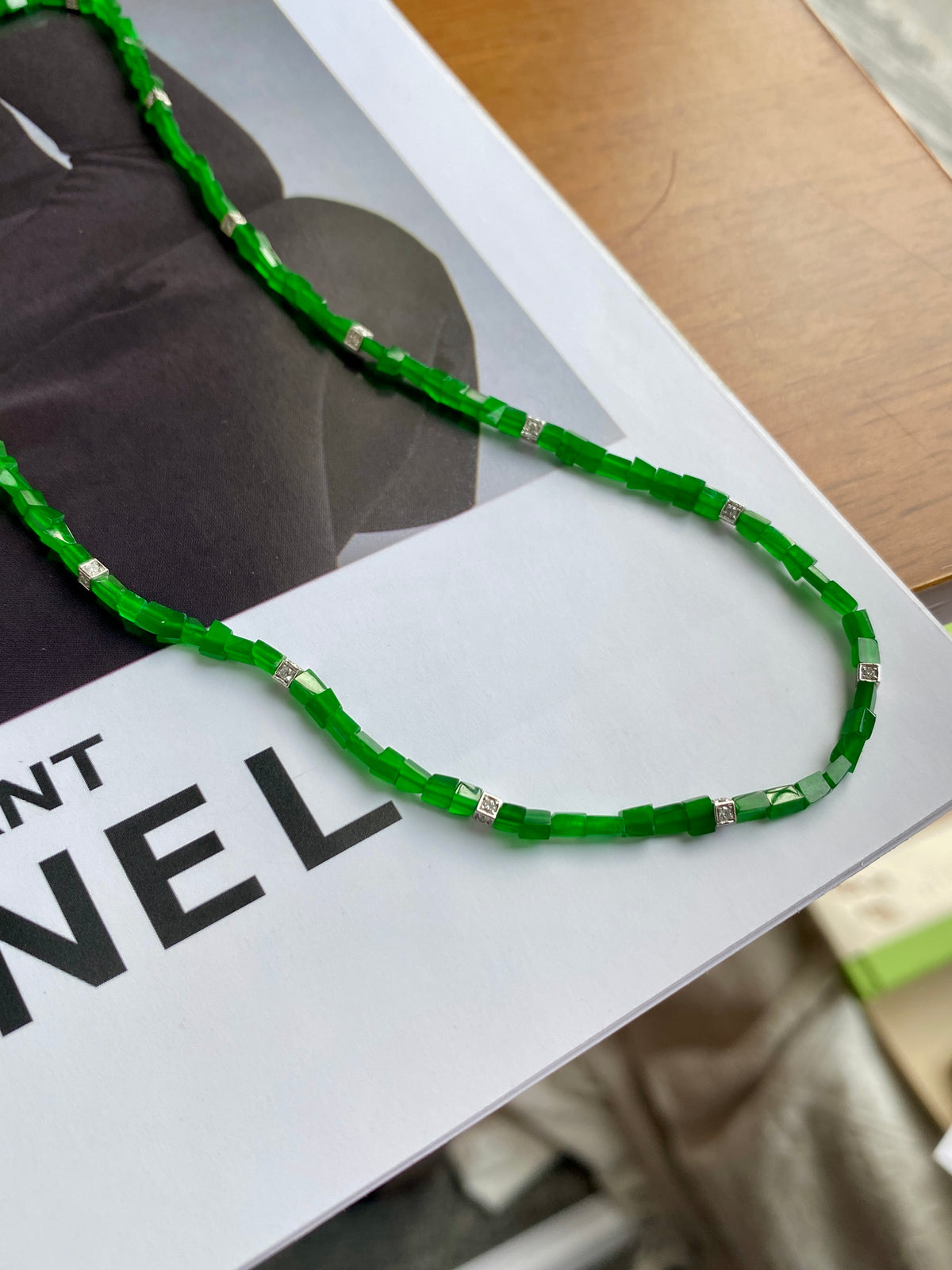 Green jadeite beaded necklace laid on white display card, silver spacer segments