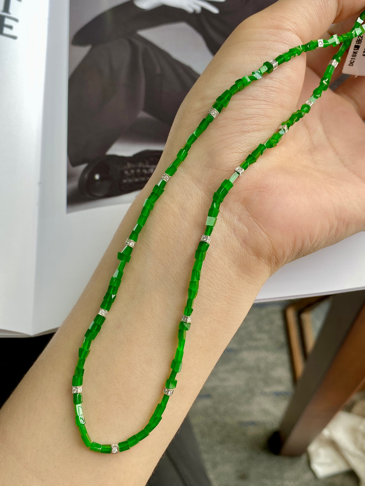 Green jadeite beaded necklace on open hand, with silver rectangular spacers