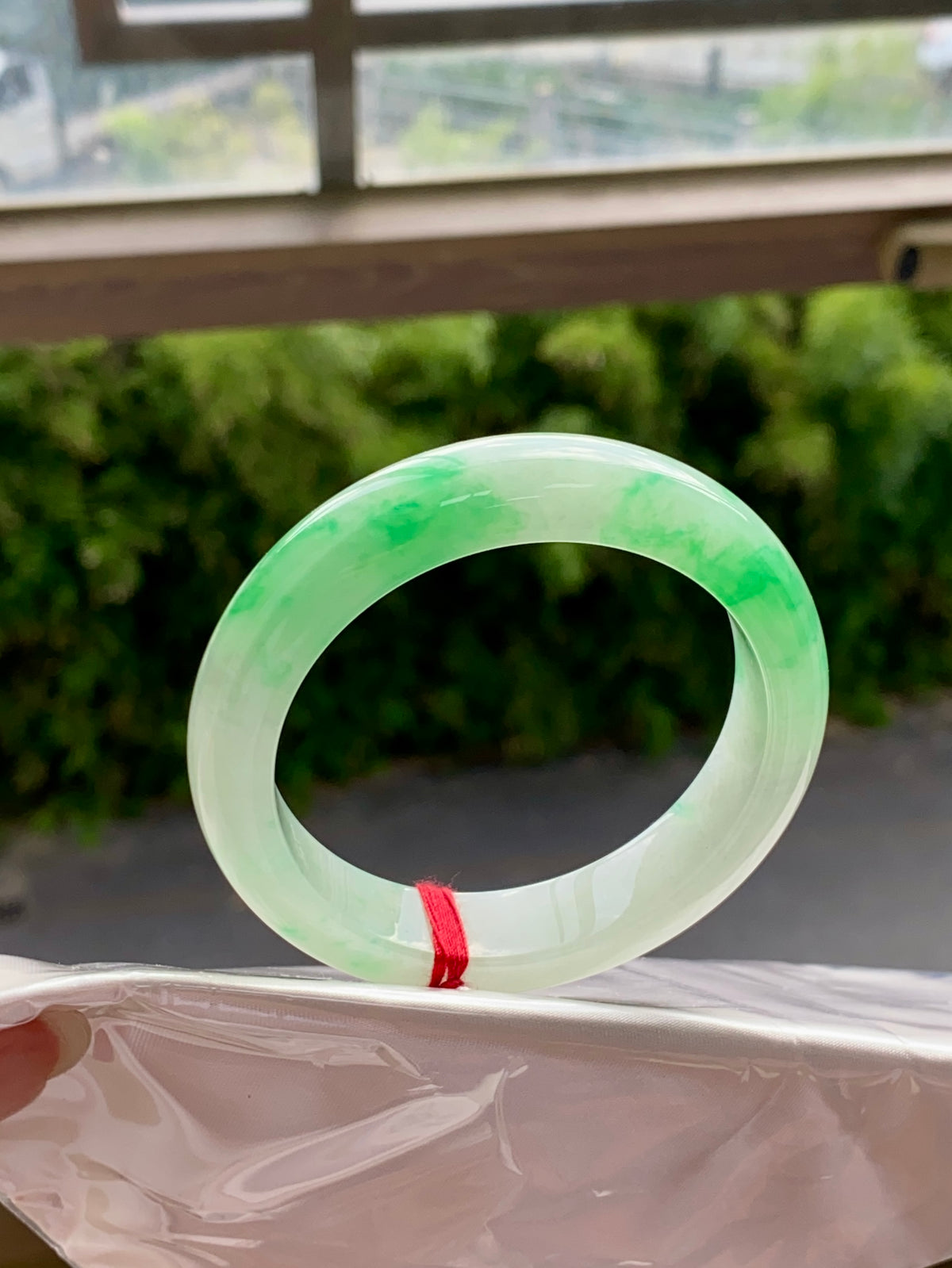 Translucent light-green jadeite bangle, full glossy ring with faint swirls and red string tie.