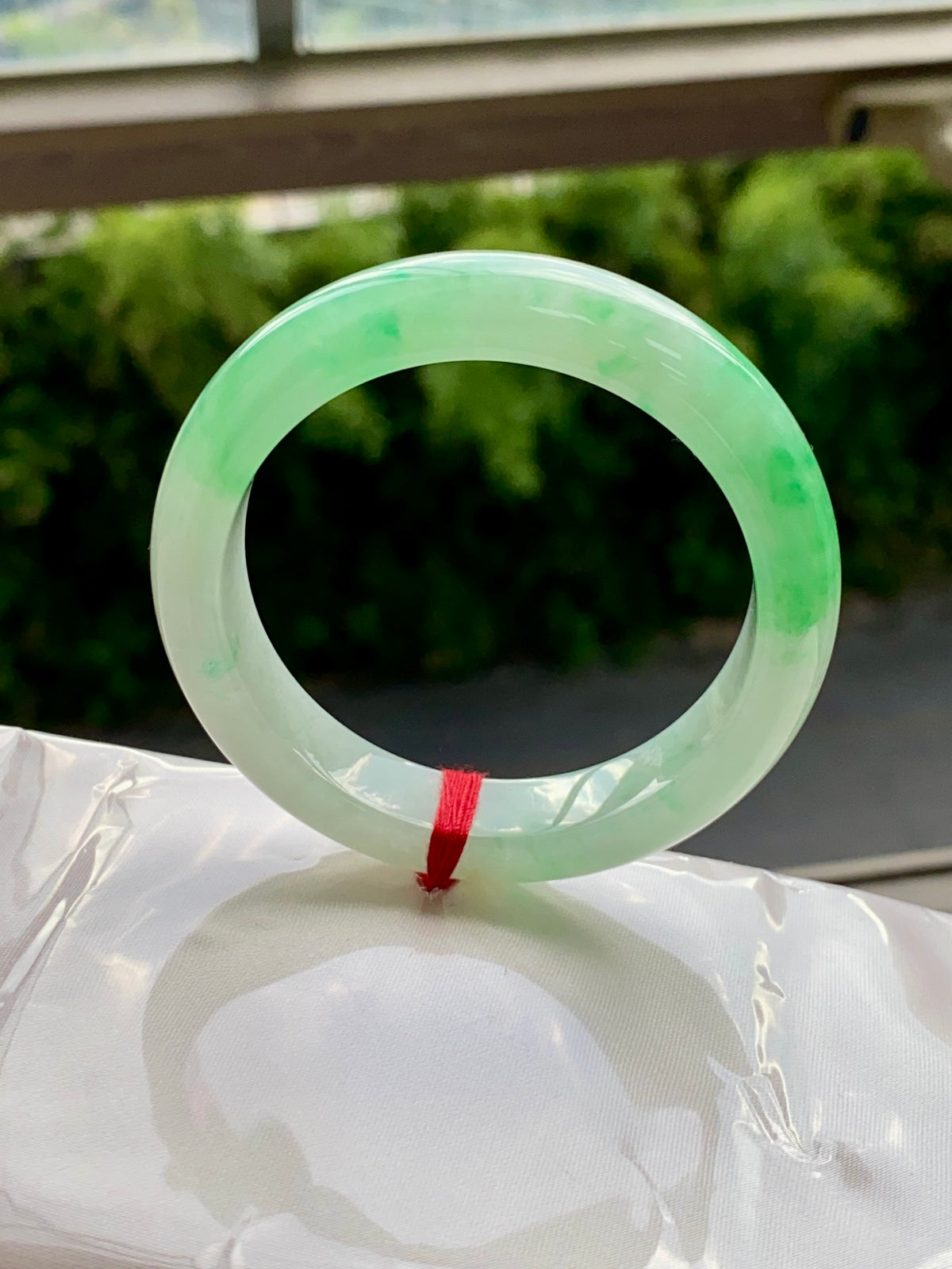 Translucent light-green jadeite bangle with faint swirls and red string tie.