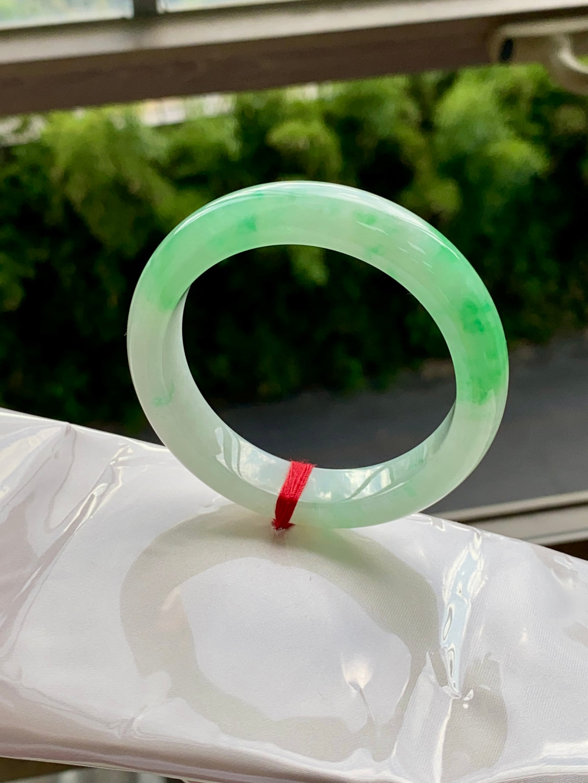 Translucent light-green jadeite bangle, glossy ring with faint swirls and red string tie.