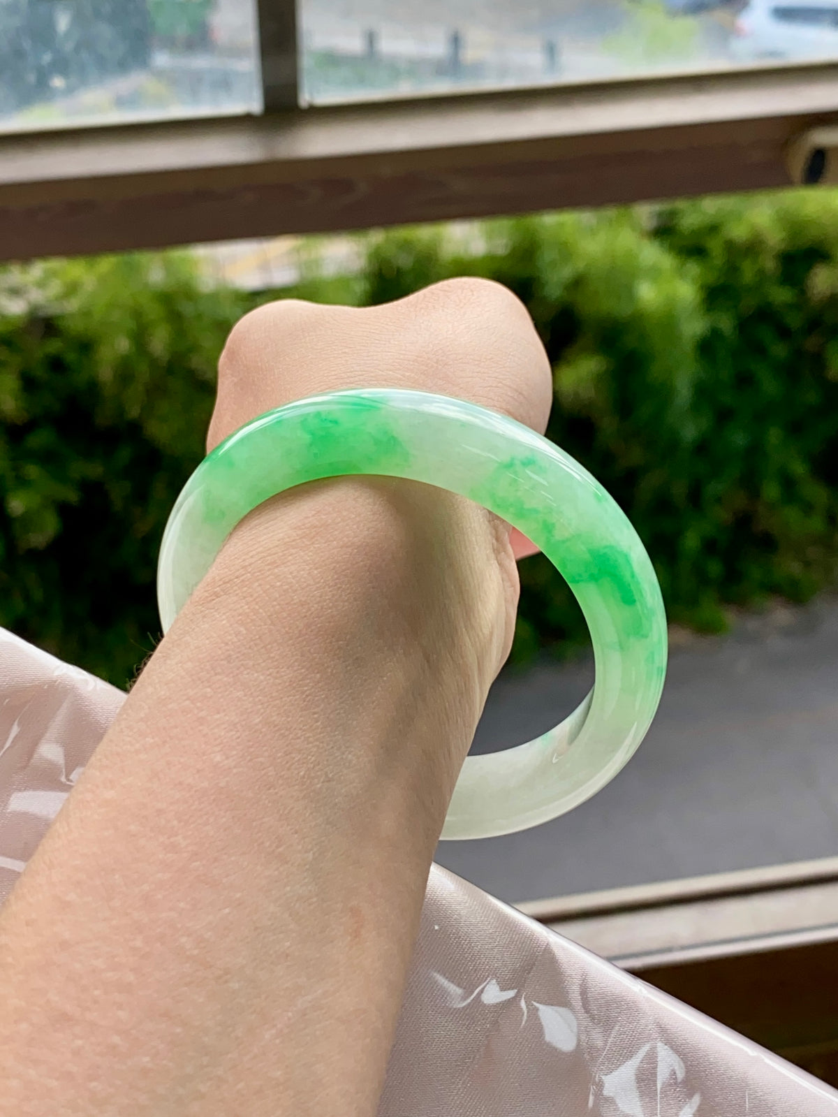 Translucent light-green jadeite bangle on wrist, faint swirls with red string tie.