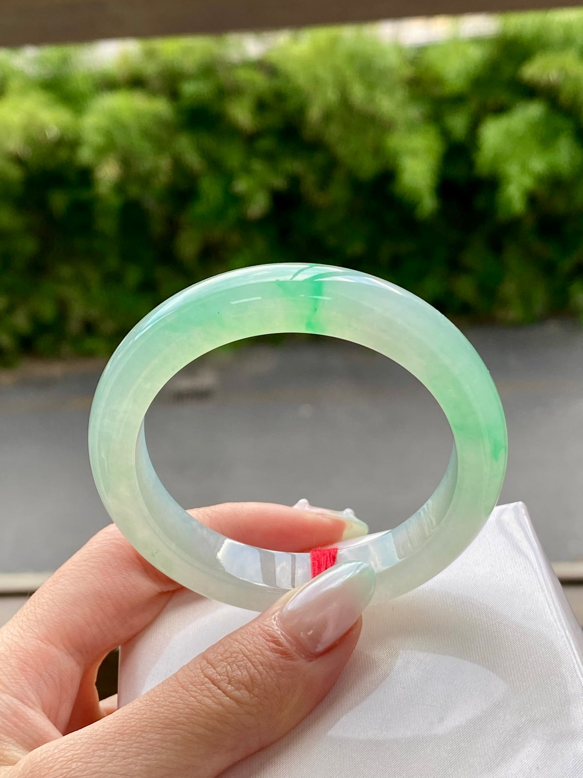 Translucent light jadeite bangle with smooth circular band, held in front of box