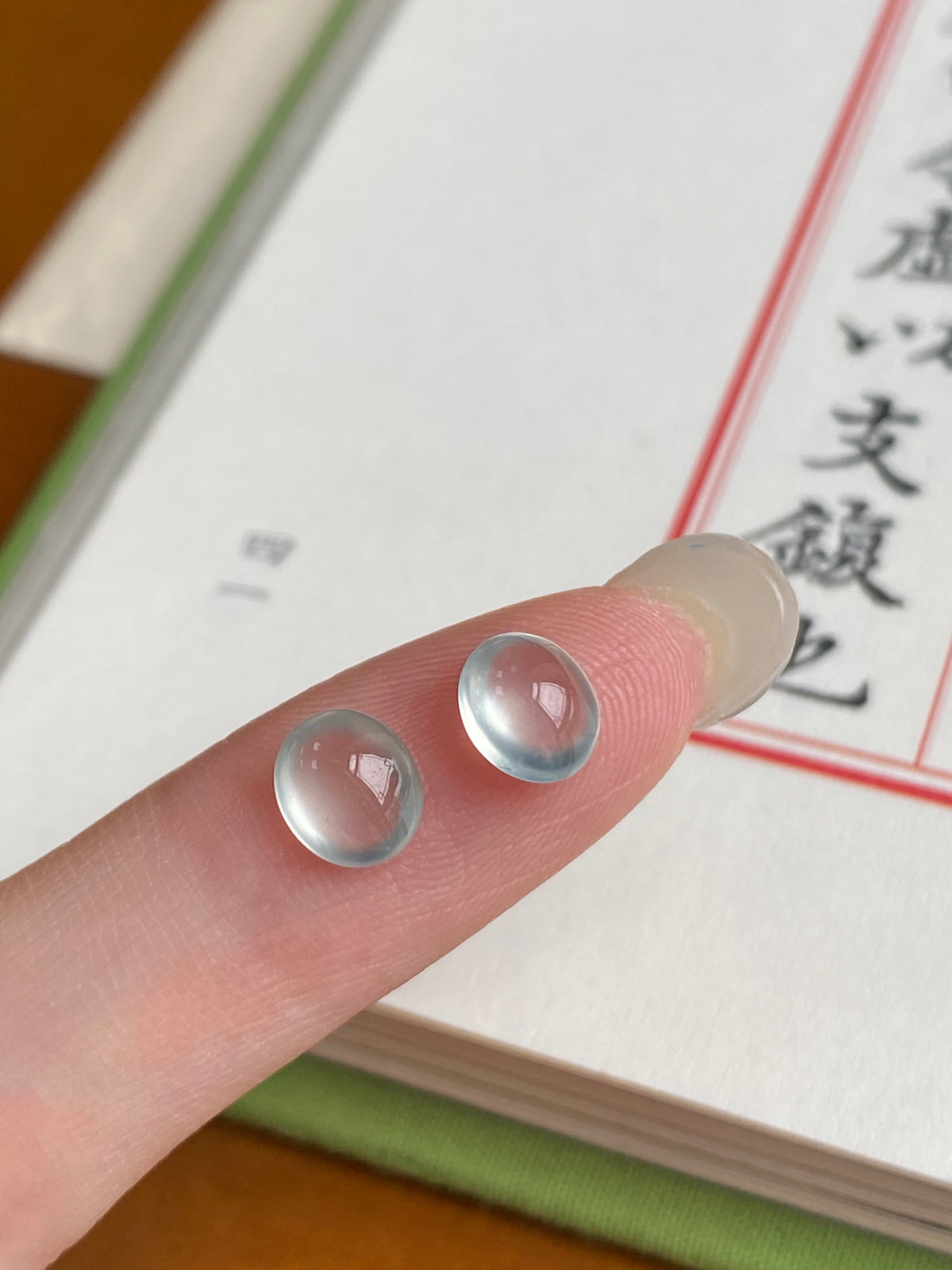 Round jadeite cabochon pair, domed pale blue, unmounted; on fingertips close