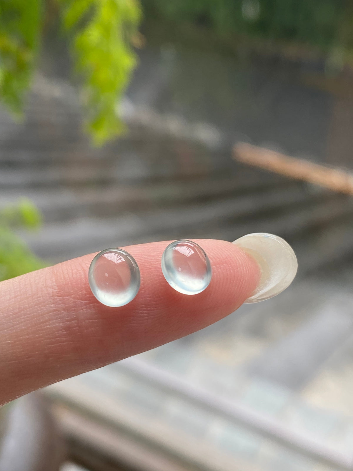 Domed round jadeite cabochon pair, pale blue, unmounted; close-up on fingers