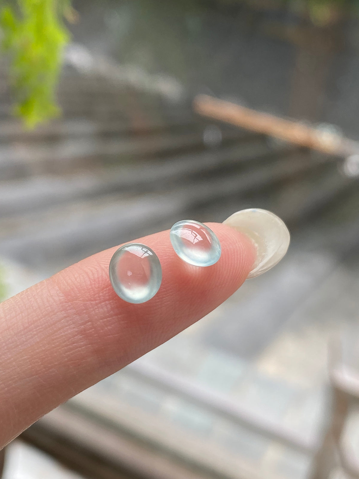 Round jadeite cabochon pair, domed pale blue, unmounted; shown on fingers
