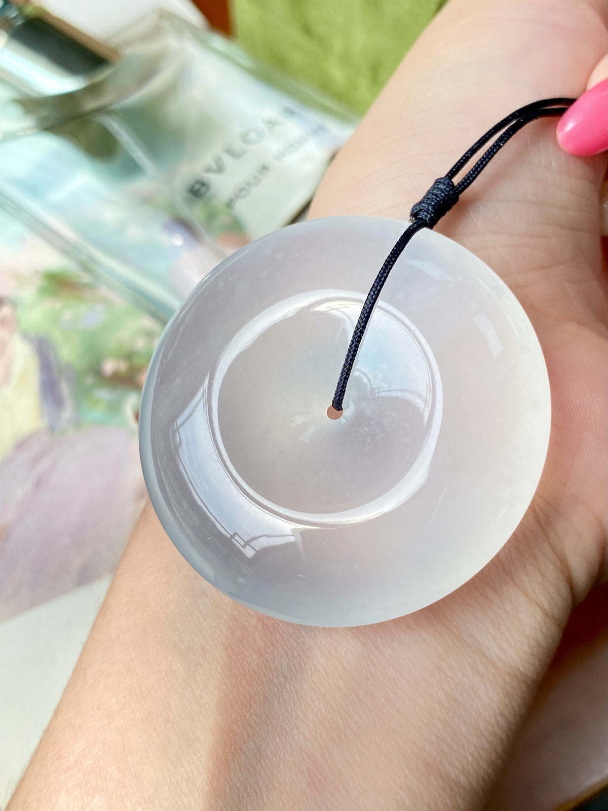 Icy white jadeite donut with black cord held in an open hand
