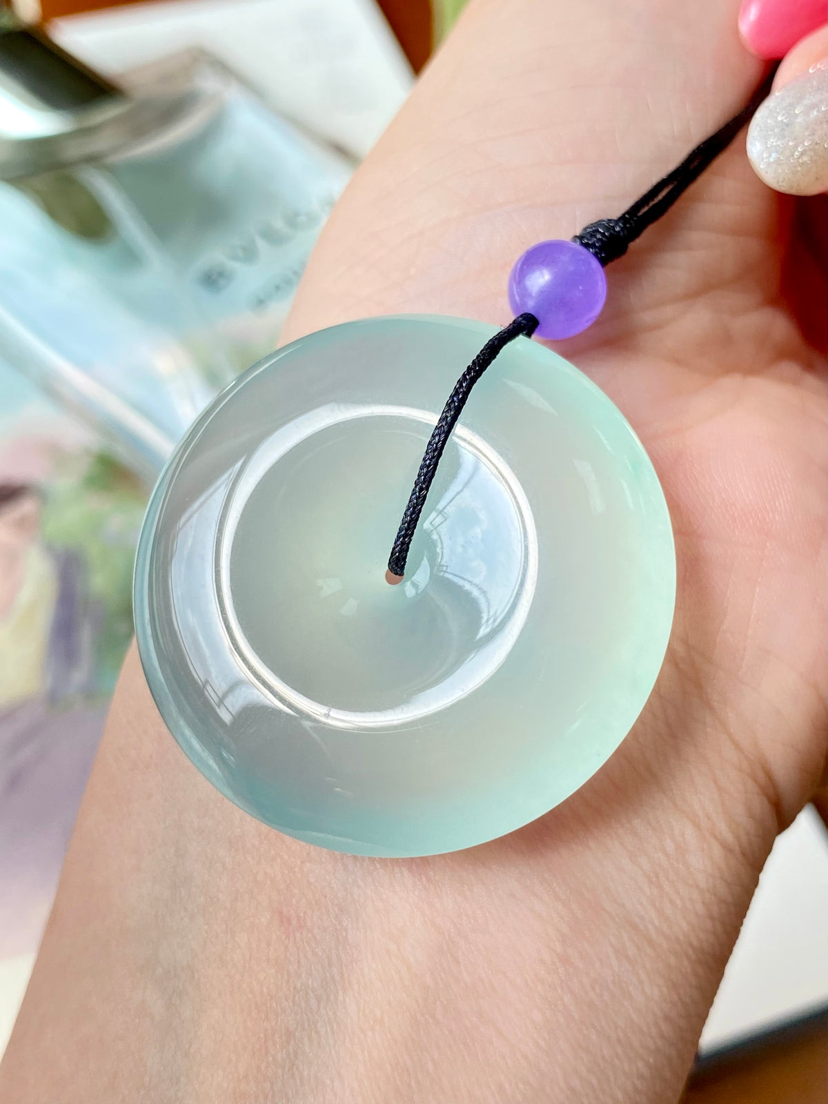 Mint green jade disc pendant held in hand, black cord with purple bead