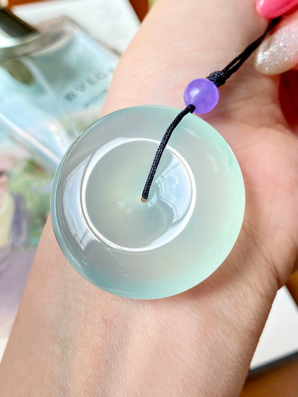 Mint green jade disc pendant with black cord loop and purple bead detail