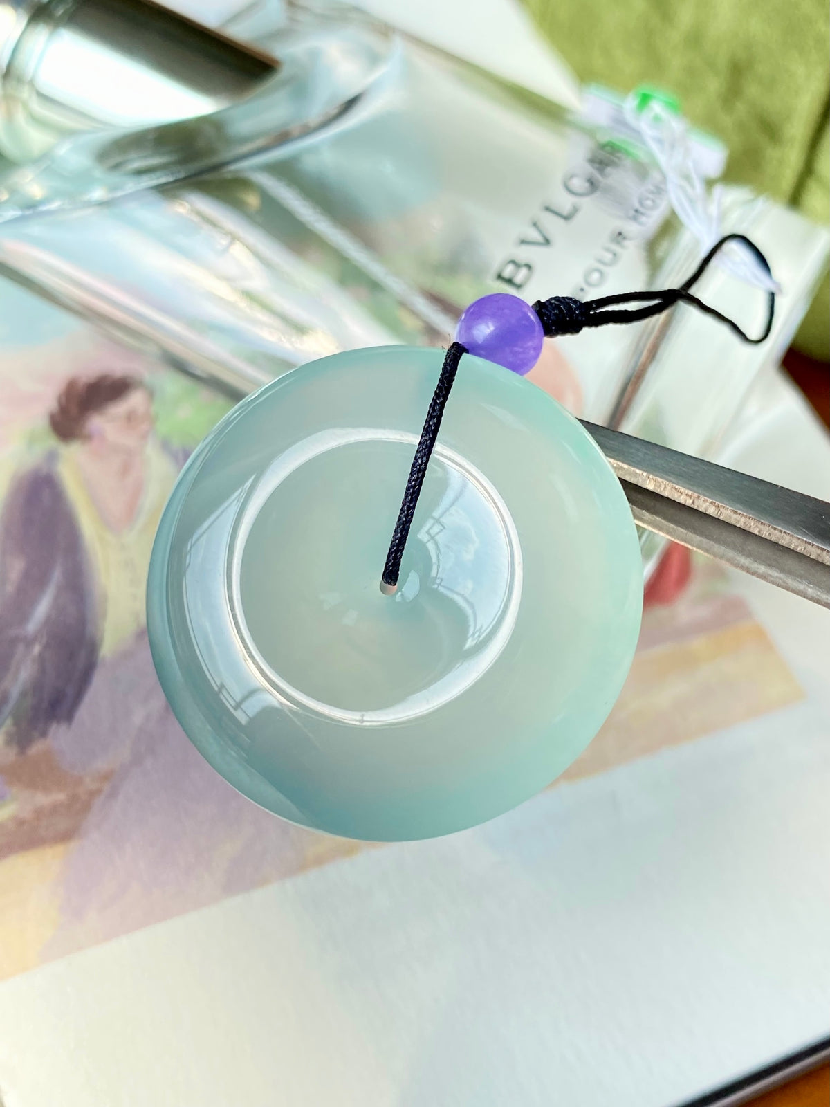 Mint green jade disc pendant with black cord, purple bead, and metal safety clip