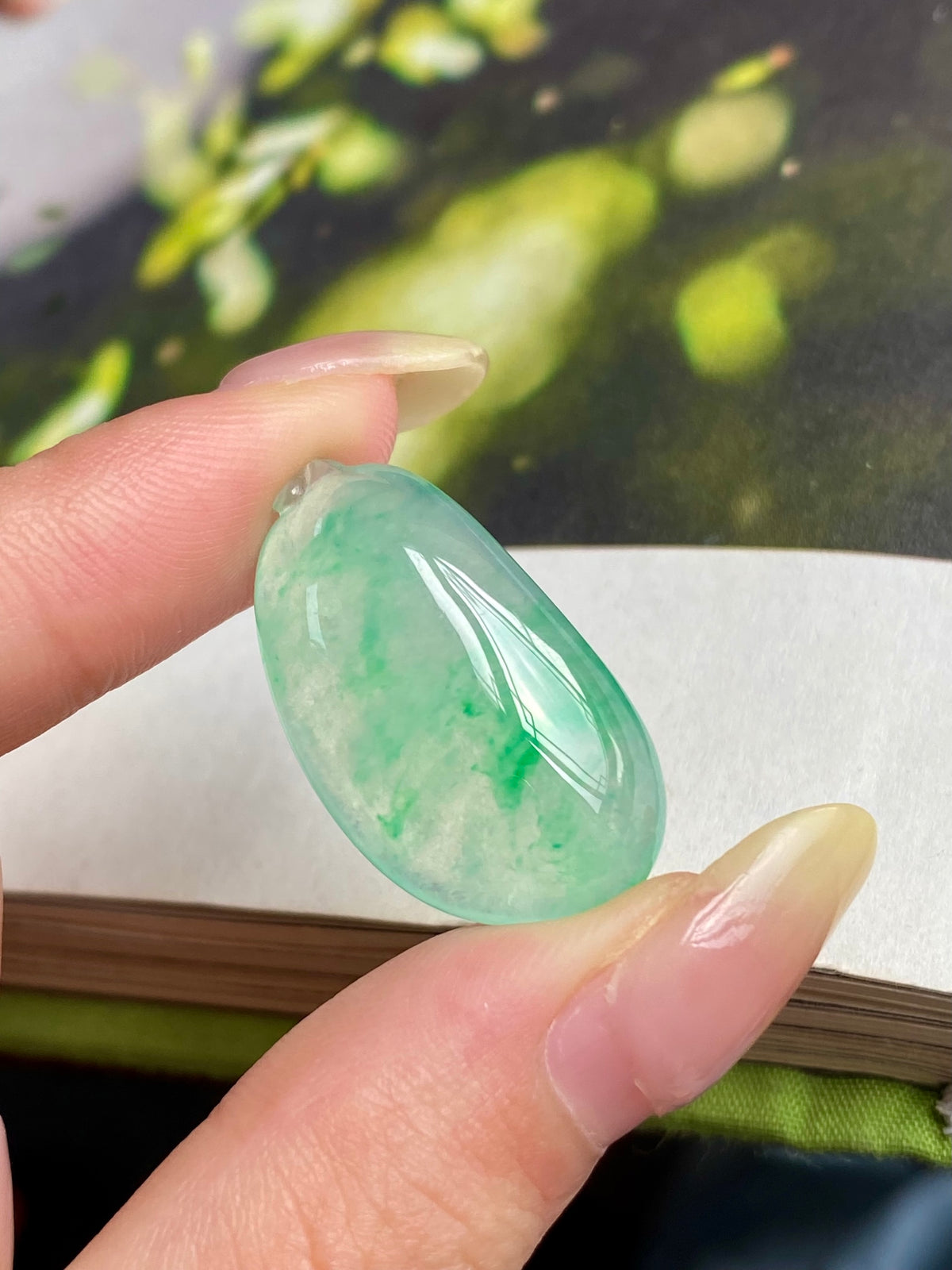 Light green jadeite melon pendant held in hand, oval teardrop with loop bail