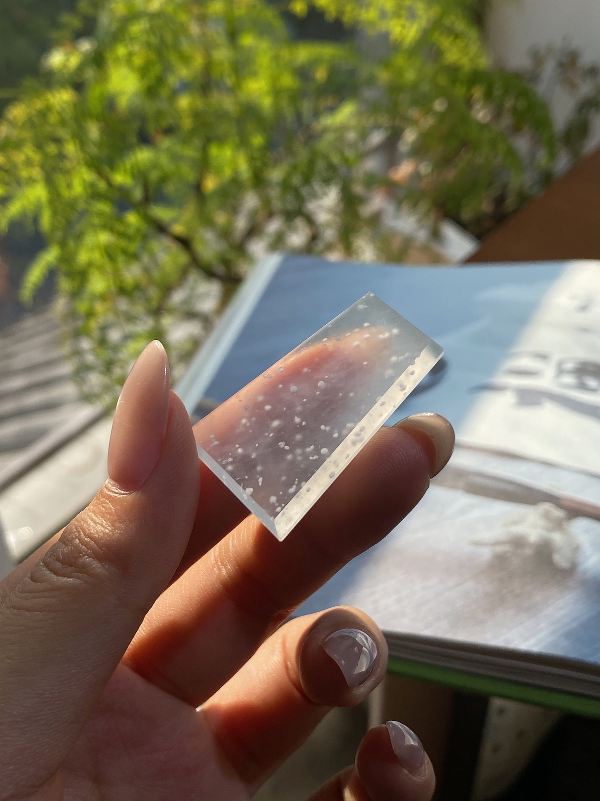 Jadeite rough stone tablet with lavender speckled inclusions, held in hand outdoors