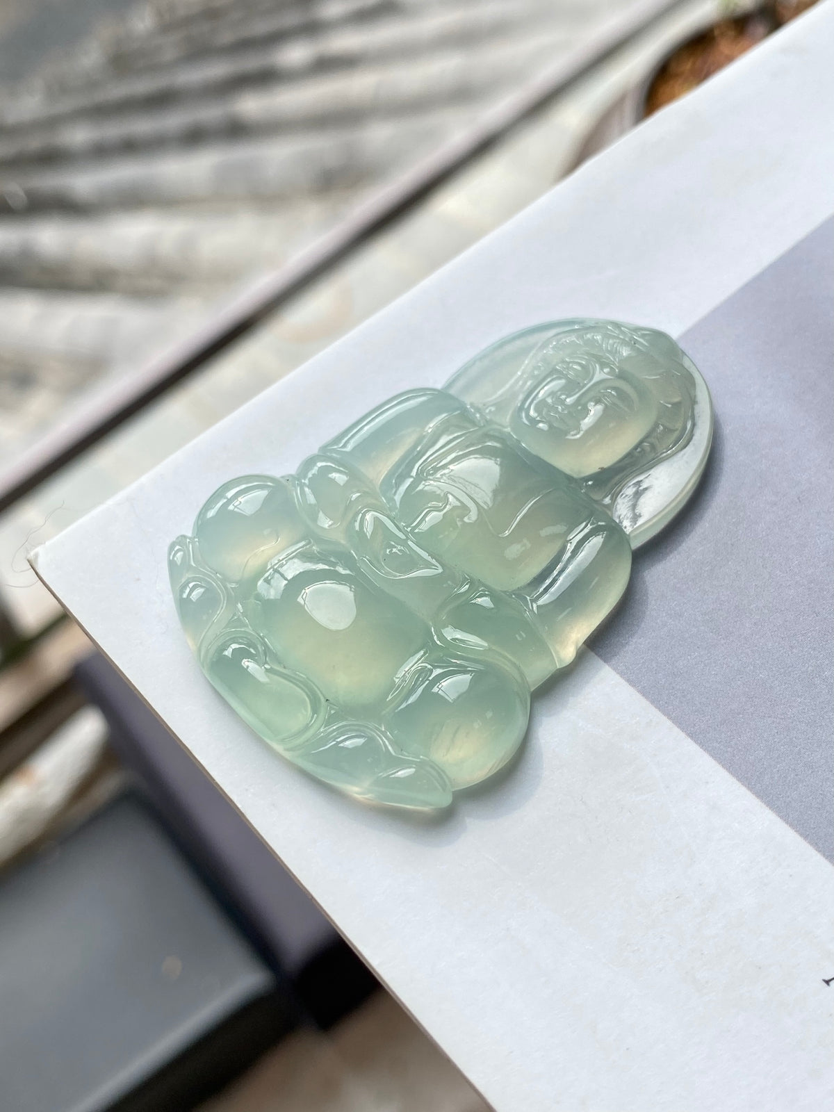 Light green Guanyin jadeite pendant lying on display card, carved seated figure