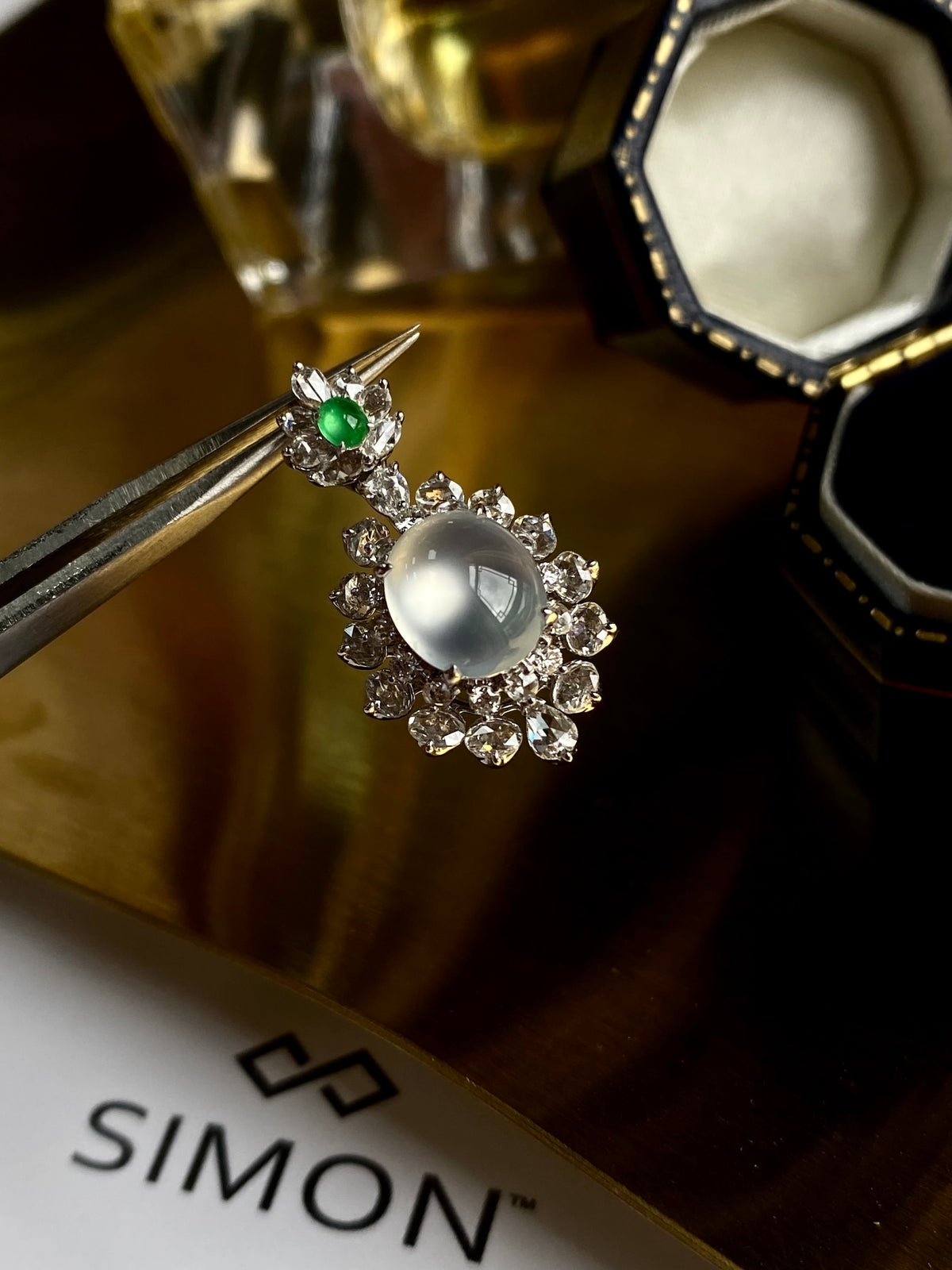 Silver-tone pendant with round white cabochon, green accent stone, and rhinestone halo