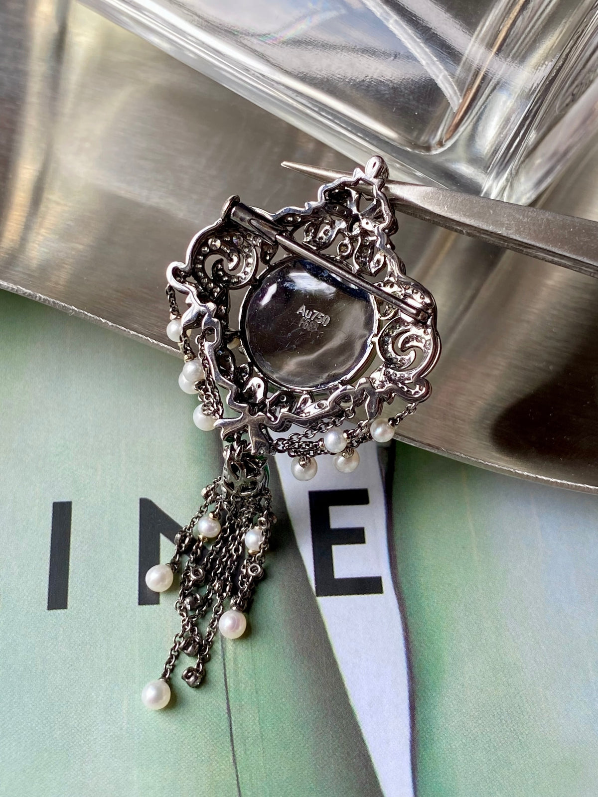 Ornate round brooch with dark center stone and dangling pearls